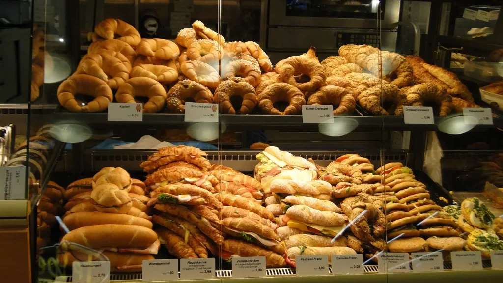 Perfeito vitrinismo de padaria repleta de variedades de pães e sanduíches, com etiquetas de preços em primeiro plano.