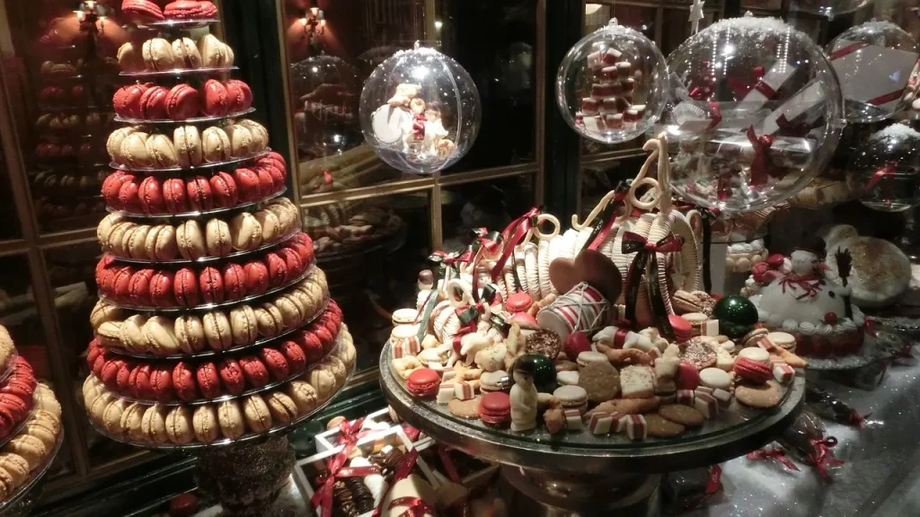 Exibição de doces temáticos de Natal, incluindo uma torre de macarons vermelhos e creme, vários biscoitos decorados e doces em uma montra de loja